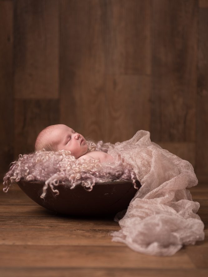 newborn baby sleeping in wooden bowl