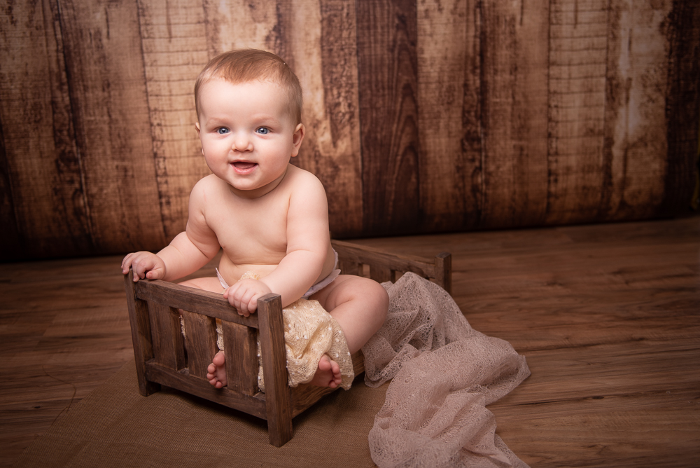 milestone sitter session boy sitting on wooden bed